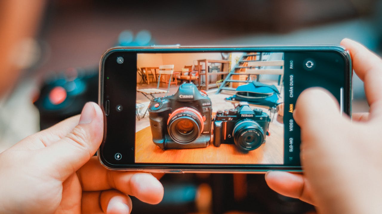 Person photographing DSLR and vintage cameras with smartphone indoors.