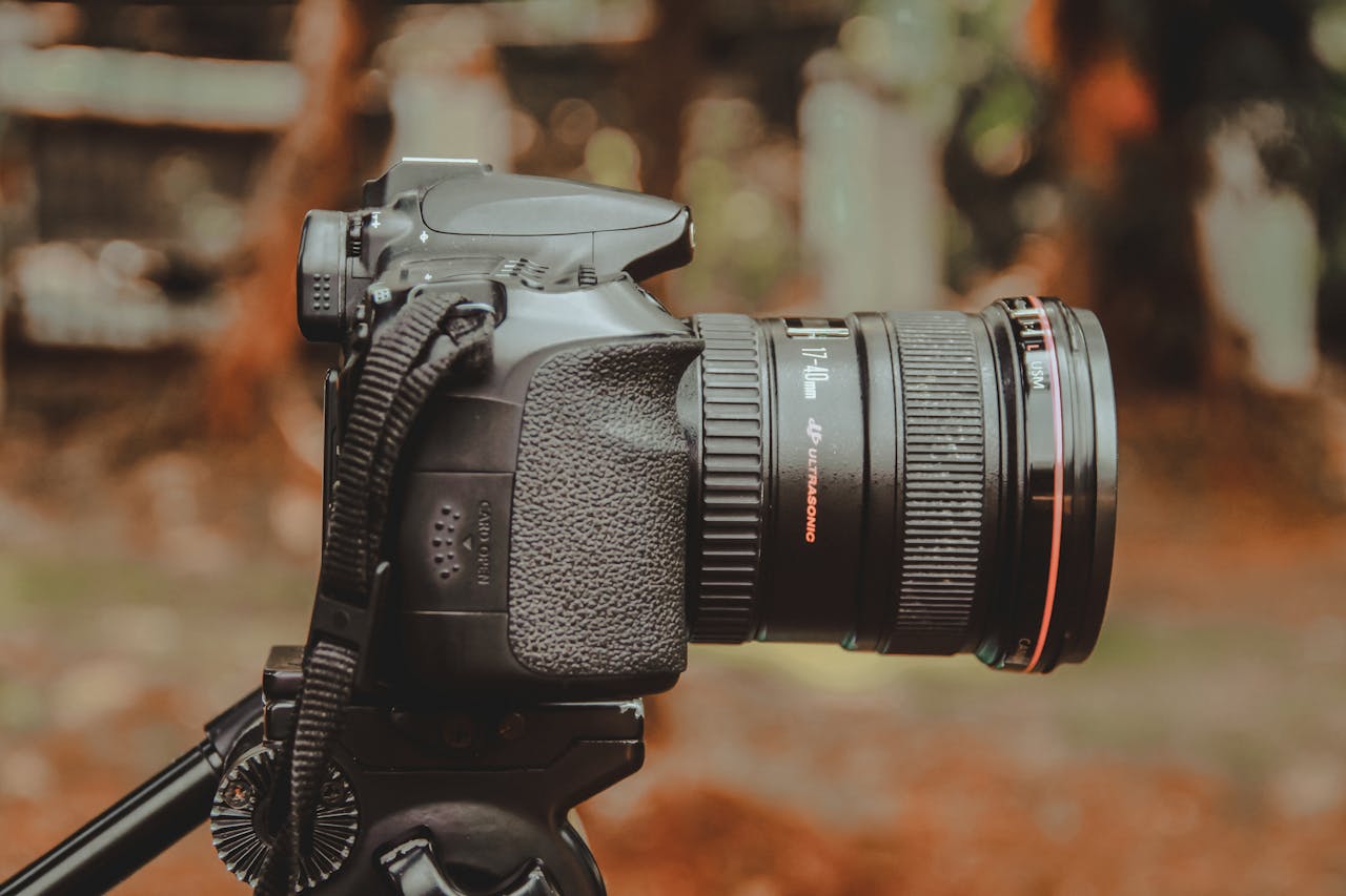 Close-up of a DSLR camera mounted on a tripod with a softly blurred outdoor background.