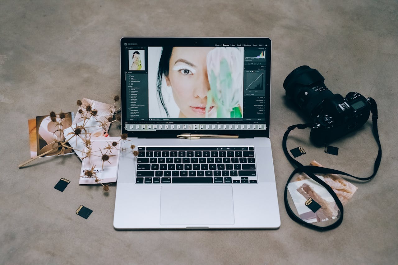 About A stylish photography setup with a laptop editing a portrait and a camera surrounded by SD cards on a concrete surface.